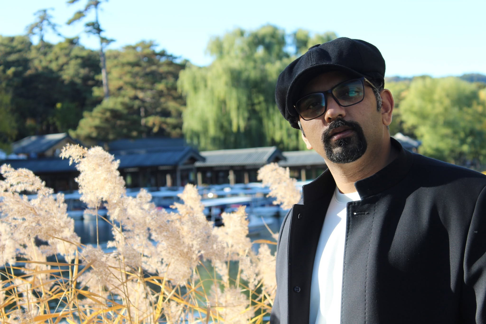 Muhammad Awais wearing a navy suit and grey cap, photographed outdoors among palm trees